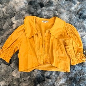 Honey colored, puffed sleeves, cropped, button down, collar. Perfect for summer!